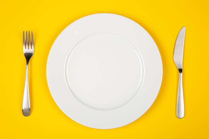 Silver fork and knife on either side of white plate, on a yellow background